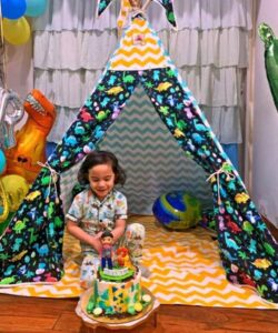 boy cutting his birthday cake in his dinosaur play tent